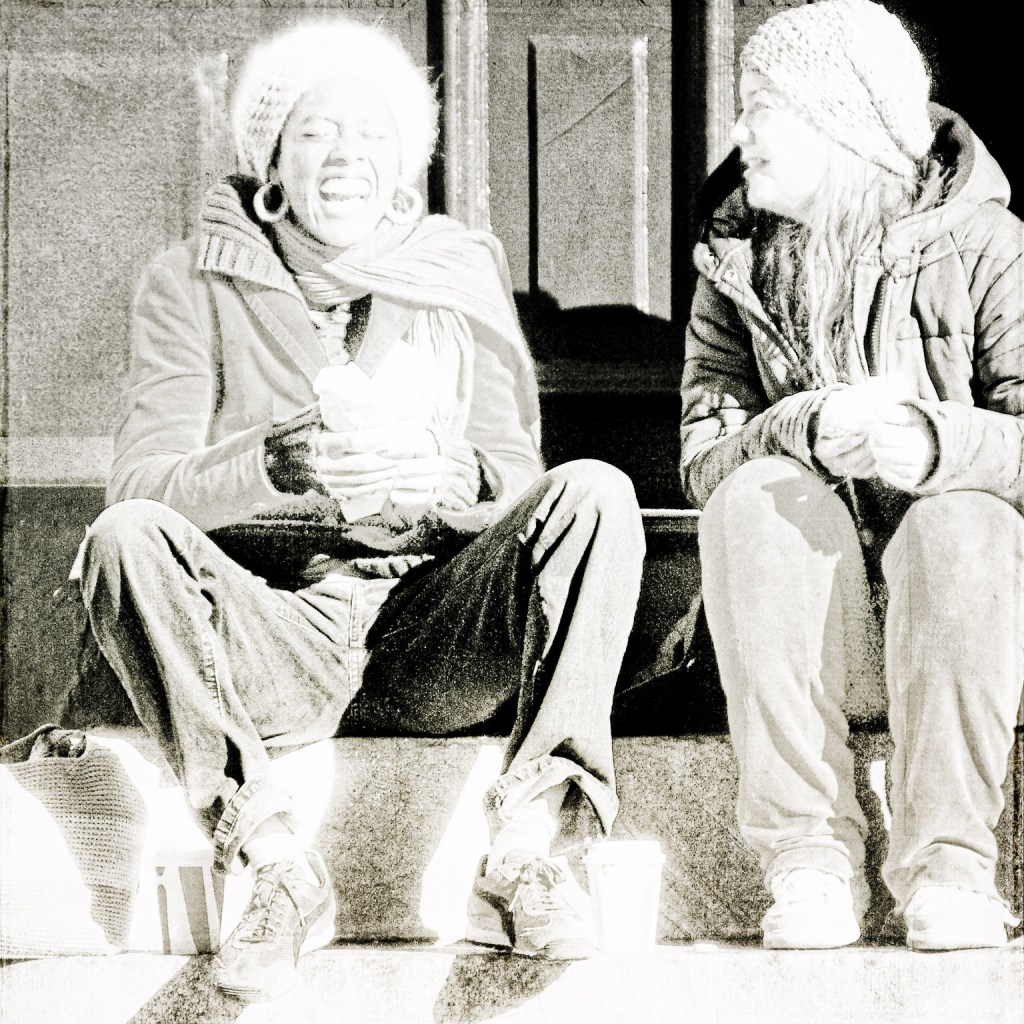 Black and white photo of a laughing teenage girl and a friend looking lovingly at her