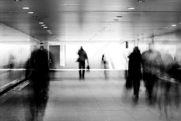 Blurred black and white photo of people moving quickly through a transit terminal building