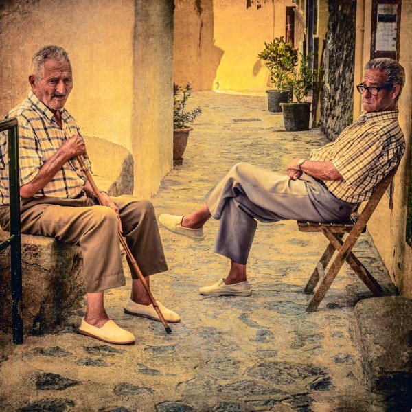 Two elderly men chatting together on a bright narrow street in an ancient village