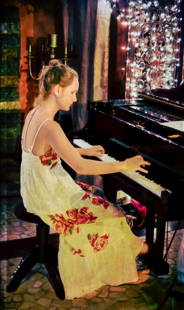 A young barefoot woman sitting still and playing an acoustic piano instrument