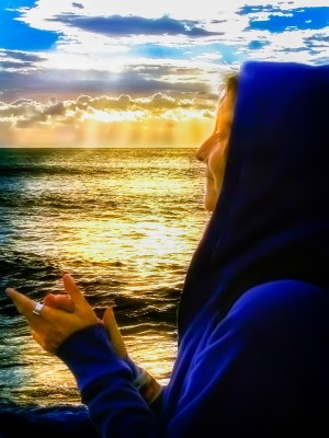 Silhouette portrait of a hooded mature woman facing the ocean at sunset
