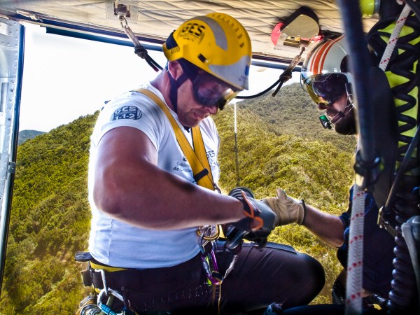 Rescue worker in a wire entering a helicopter door over a dense rainforest